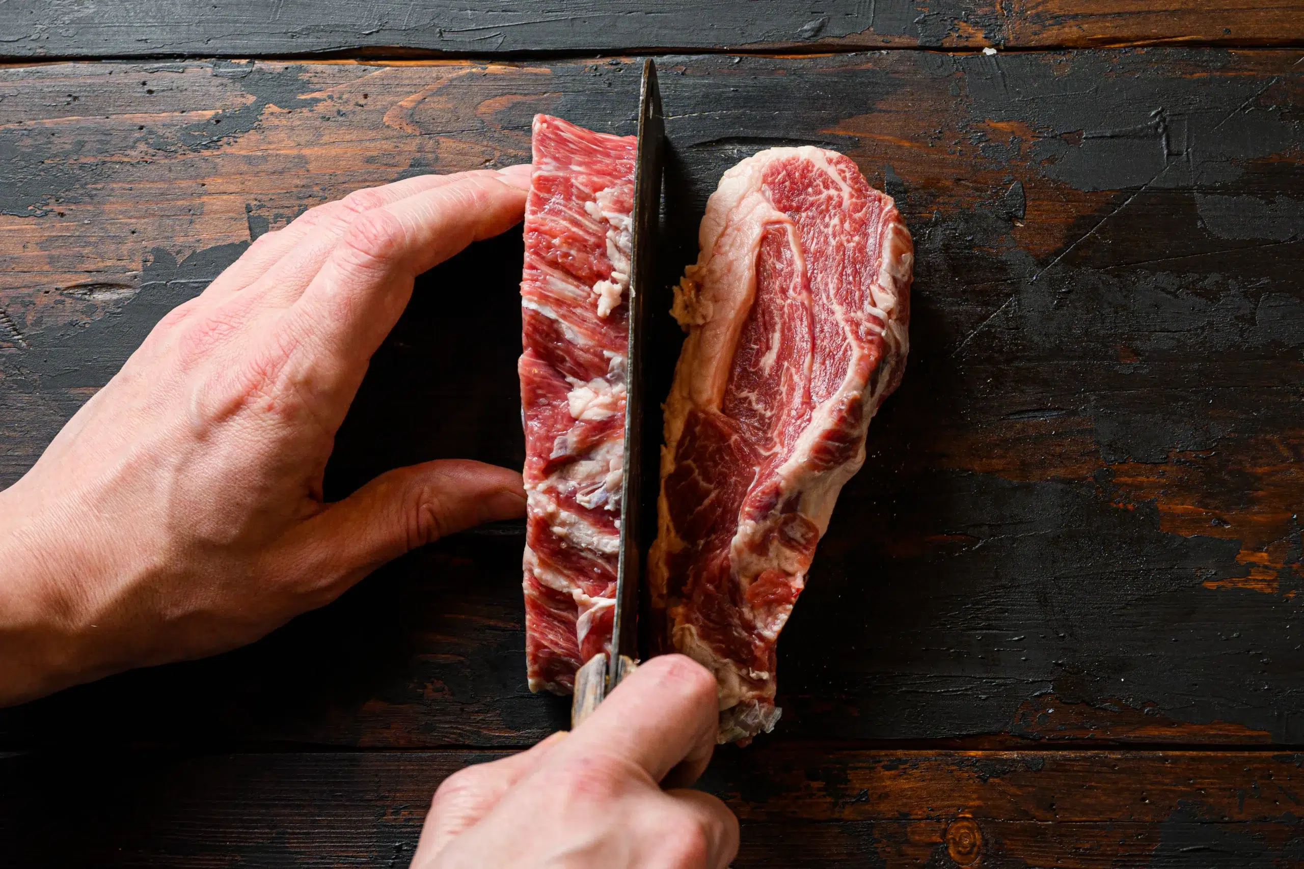 vista-superior-del-bistec-con-manos-de-carnicero-cortando-la-carne-por-la-mitad