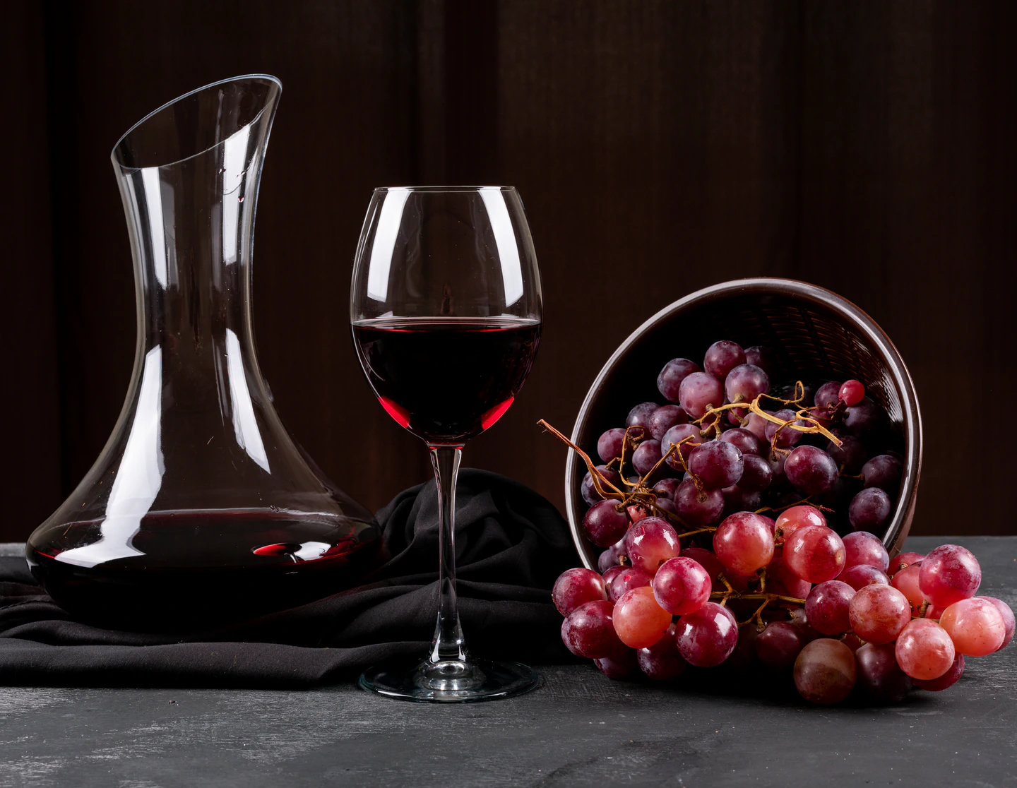 vista-lateral-de-la-jarra-con-vino-tinto-y-uva-en-horizontal-oscuro